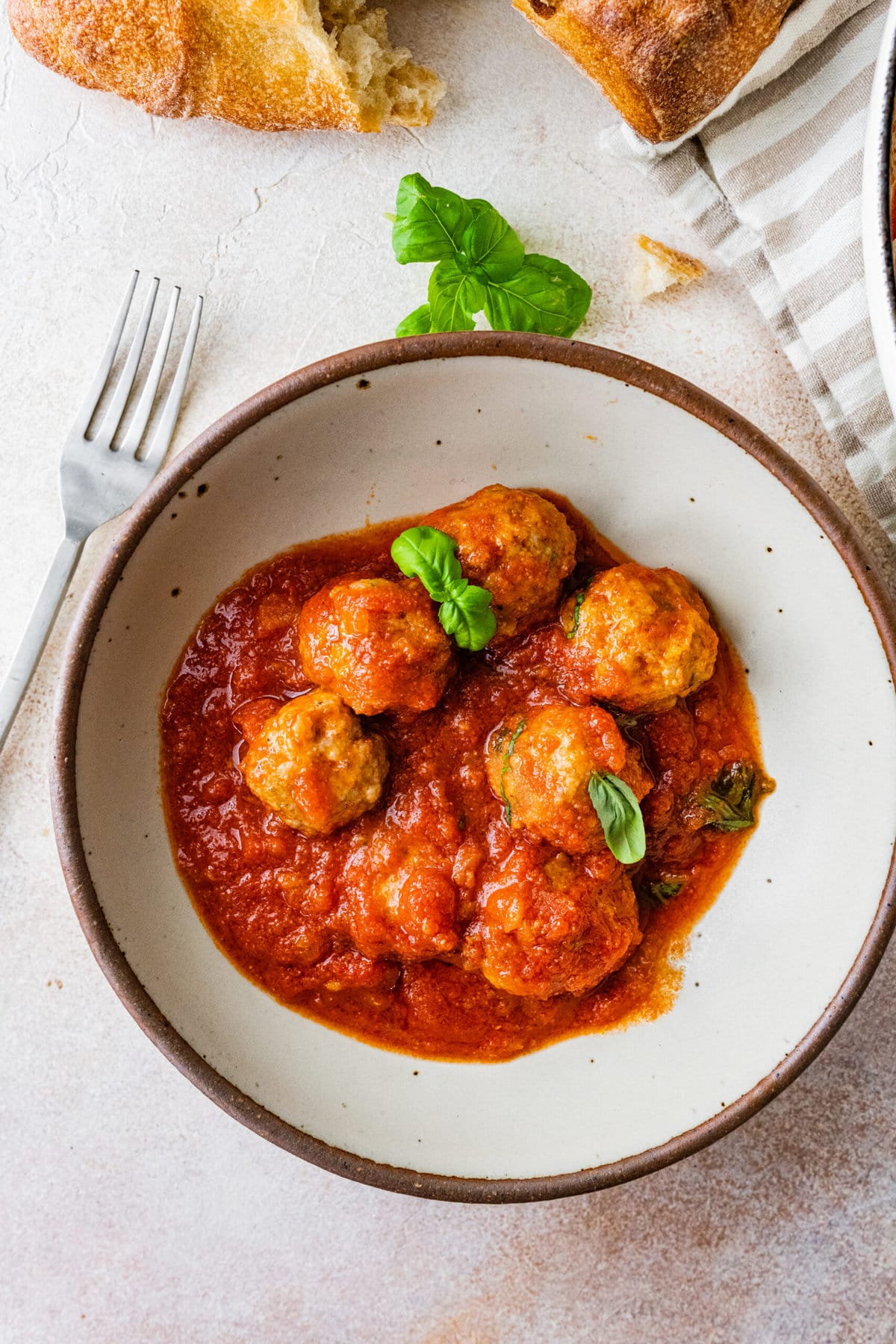 Italian sausage meatballs in a bowl with a fork. Ciabatta bread in the background.