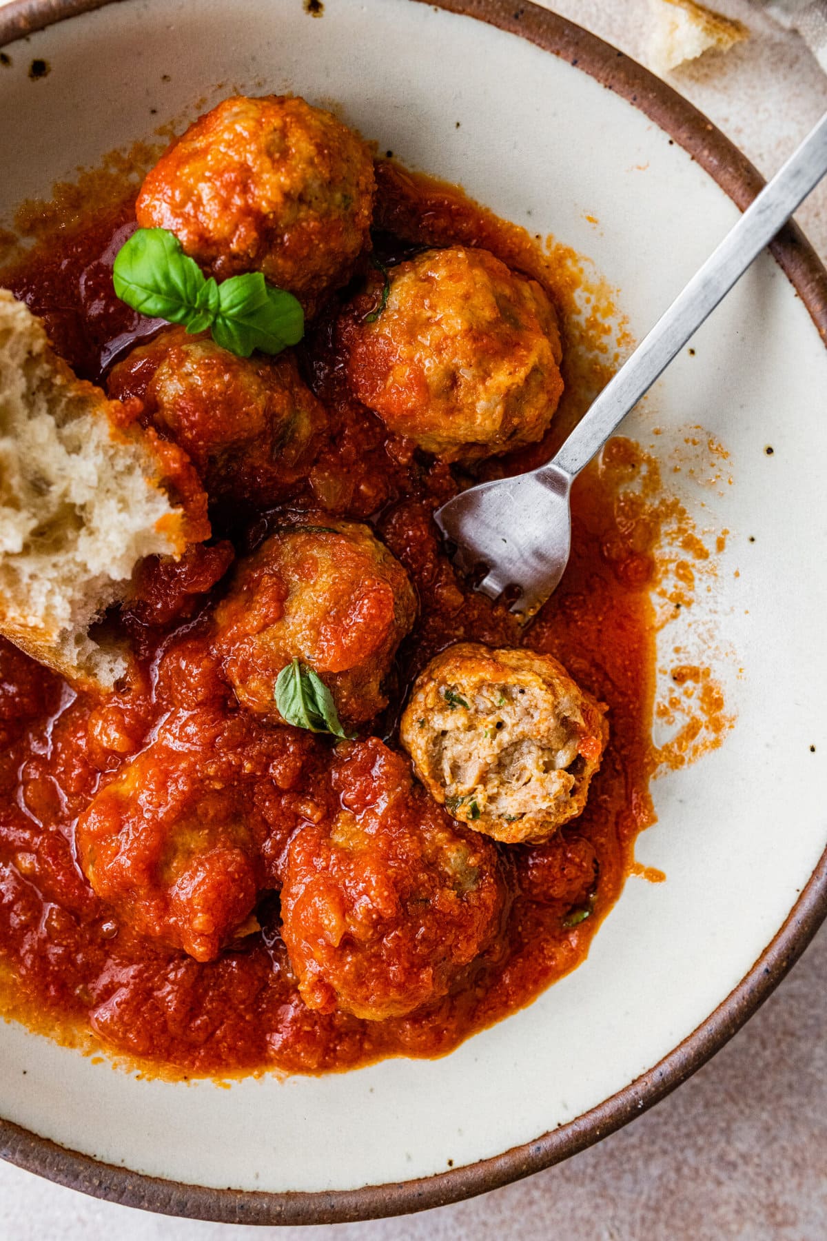 Close up of Italian sausage meatballs in a bowl pieces of broken ciabatta bread in the bowl. One bite taken from a meatball. Soft and tender interior of meatball.