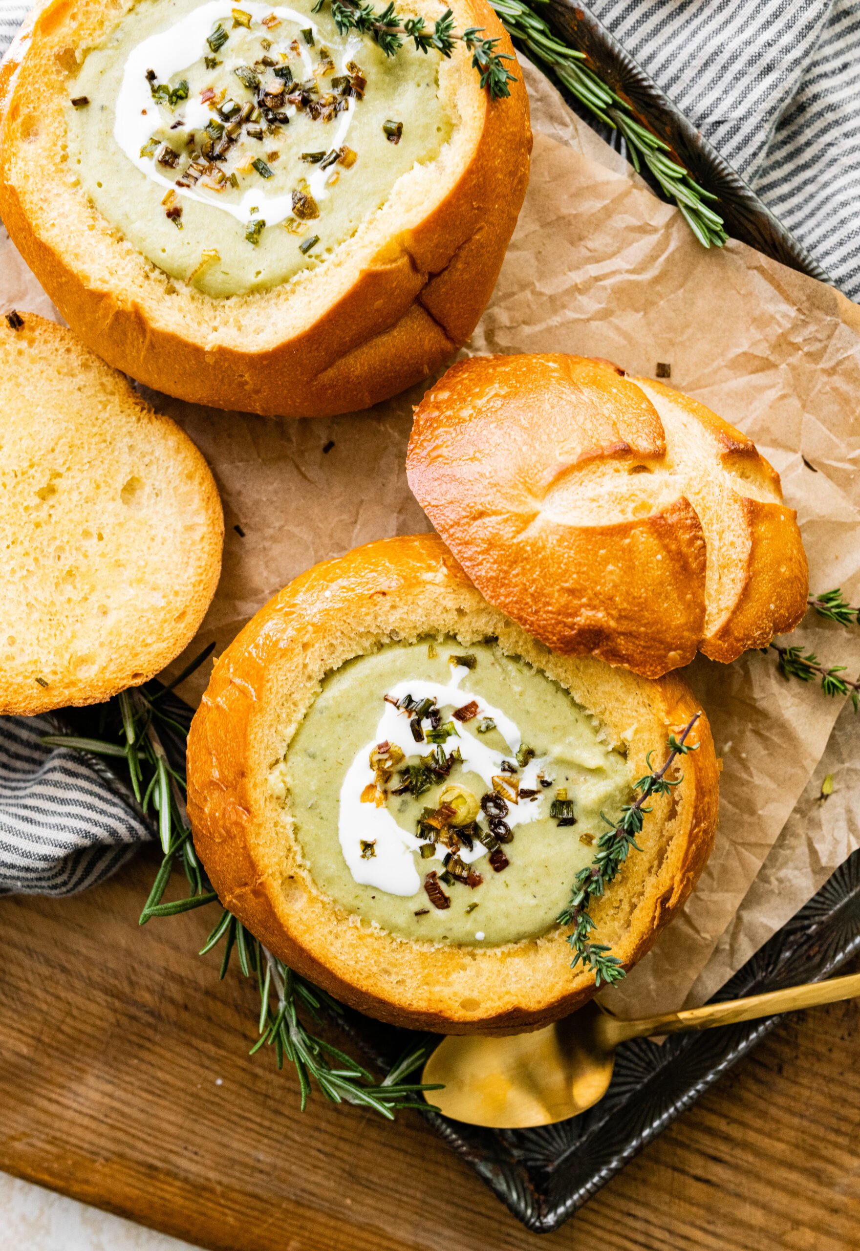 two bread bowls with no potato leek soup in the and the tops of bread bowl resting on the side on the surface.