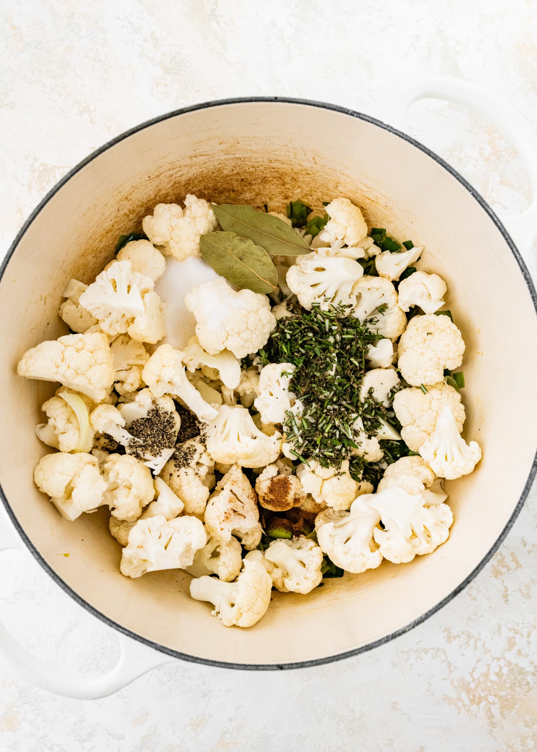 process of making No Potato Leek Soup Recipe- adding cauliflower and herbs to pot with leeks.