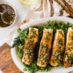 pan seared Chilean sea bass on a platter with greens and lemon slices.