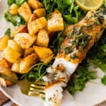 pan seared sea bass on plate with roasted potatoes on plate with green salad. Piece of fish on fork ready to eat.