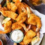 Fried shrimp on serving platter with lemon wedges, parsley, and tartar sauce. Glas of water with lemon in it.