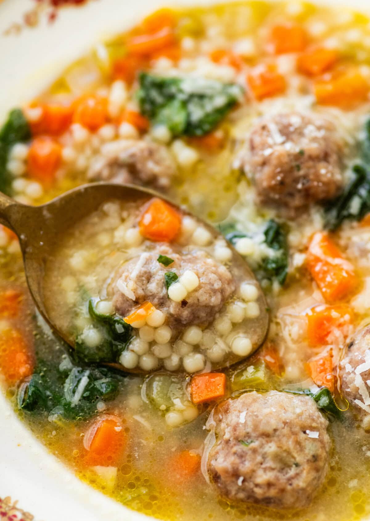 A spoon lifting up a bite of Italian wedding soup in the bowl.