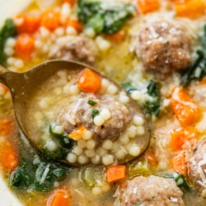 A bowl of Italian wedding soup with a spoon lifting a bite.