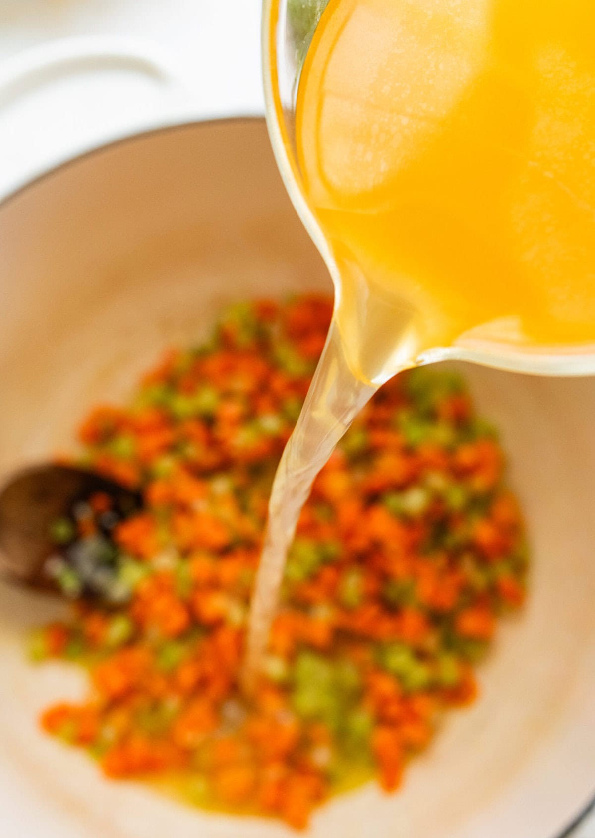 Pouring in the broth to the pot of Italian wedding soup.