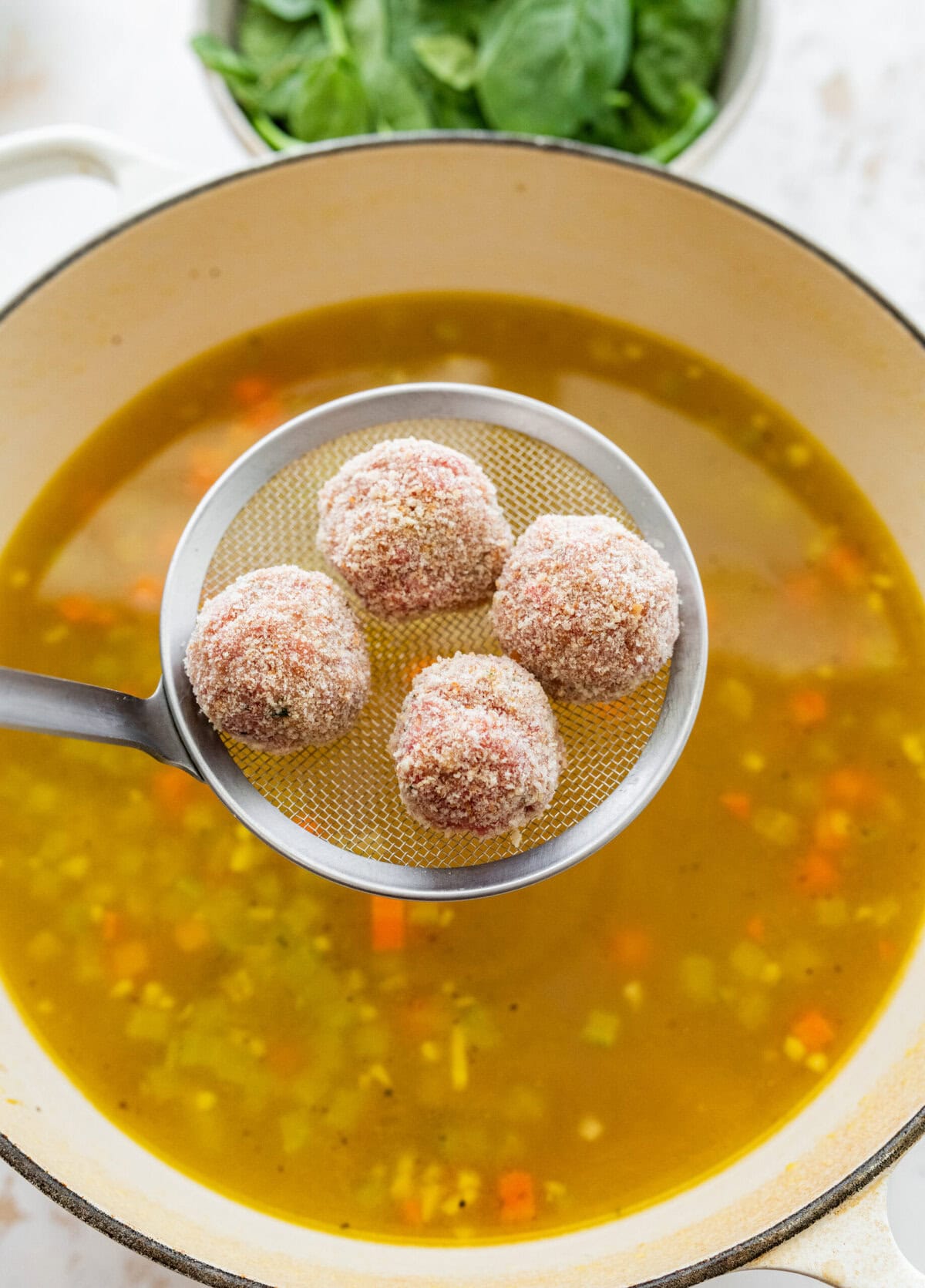 Adding meatballs to the pot of wedding soup.
