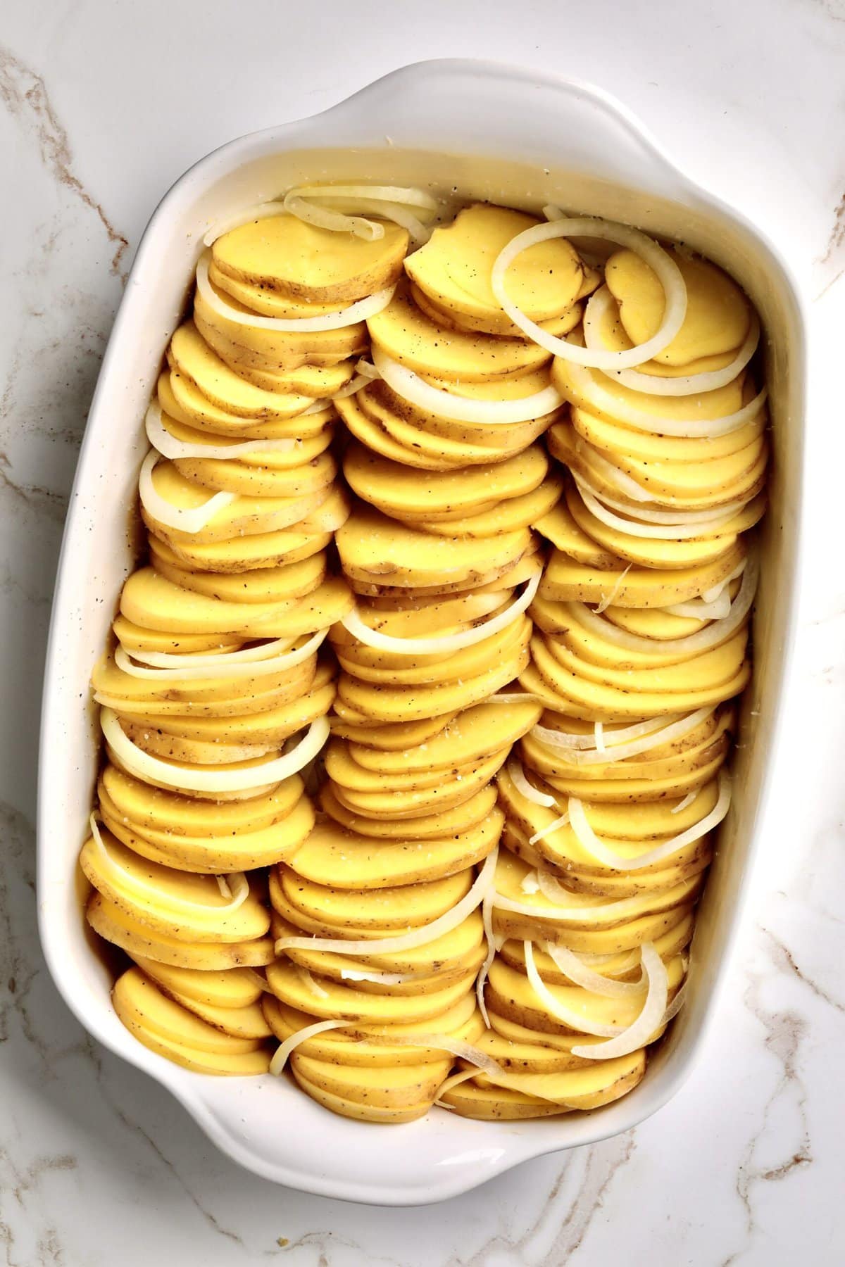 How to make Best Creamy Au Gratin Potatoes Recipe (Dad's Famous)- placing onions and potatoes in a greased baking dish.