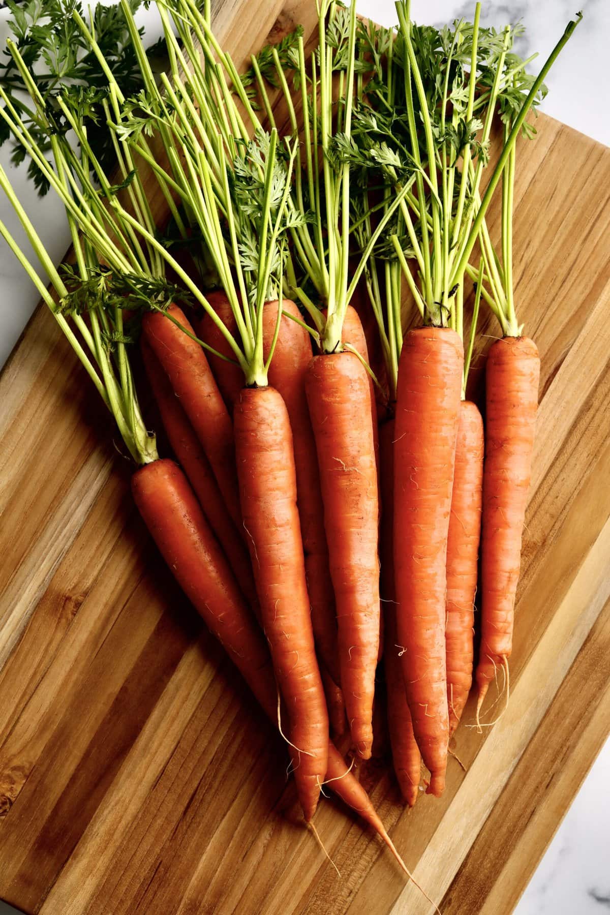 raw carrots with green stems on a cutting board.