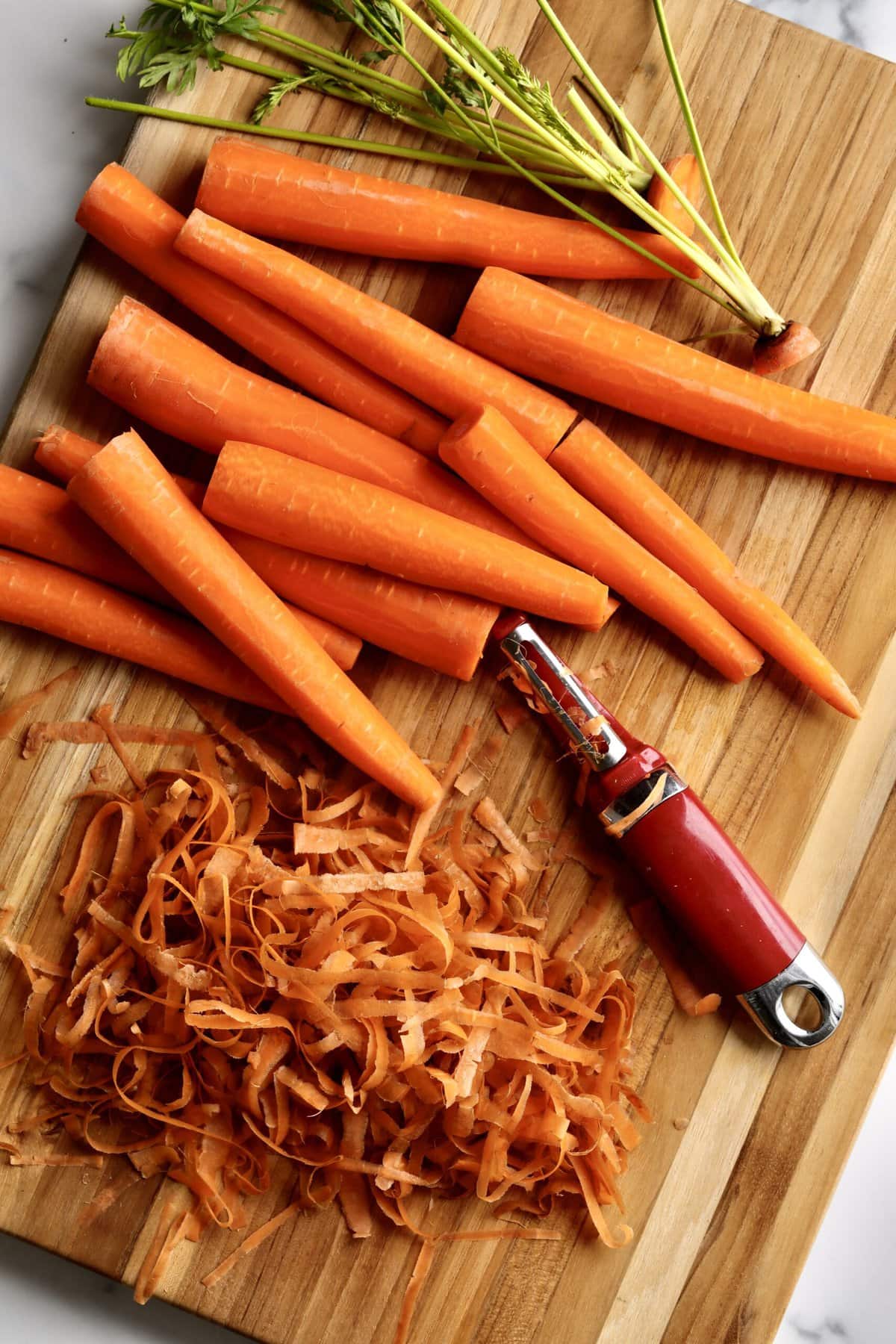 peeled carrots on a cutting board with peeler.