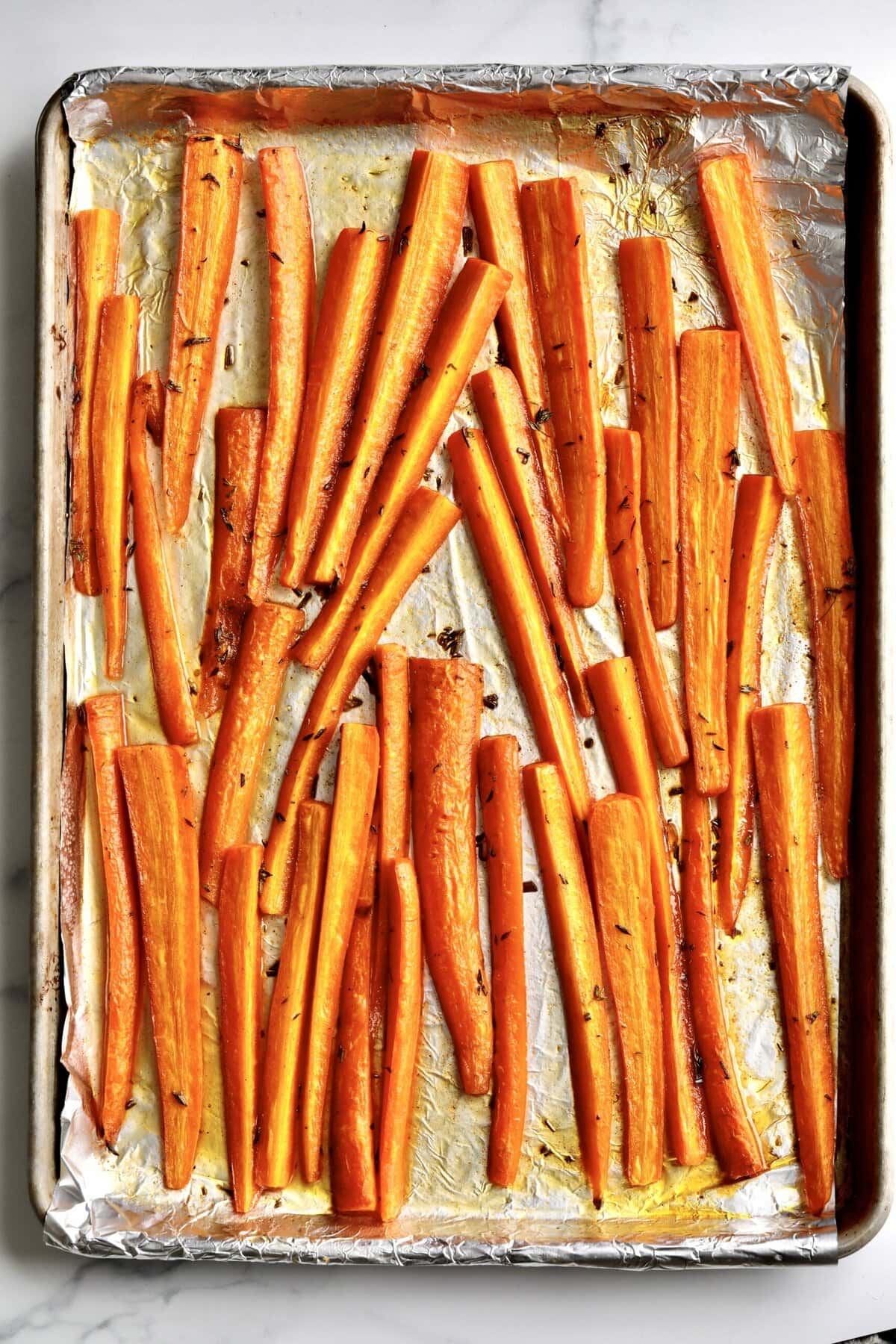 How to makeBest Honey Glazed Carrots Recipe (Oven Roasted)- finished carrots on a baking sheet lined with foil.