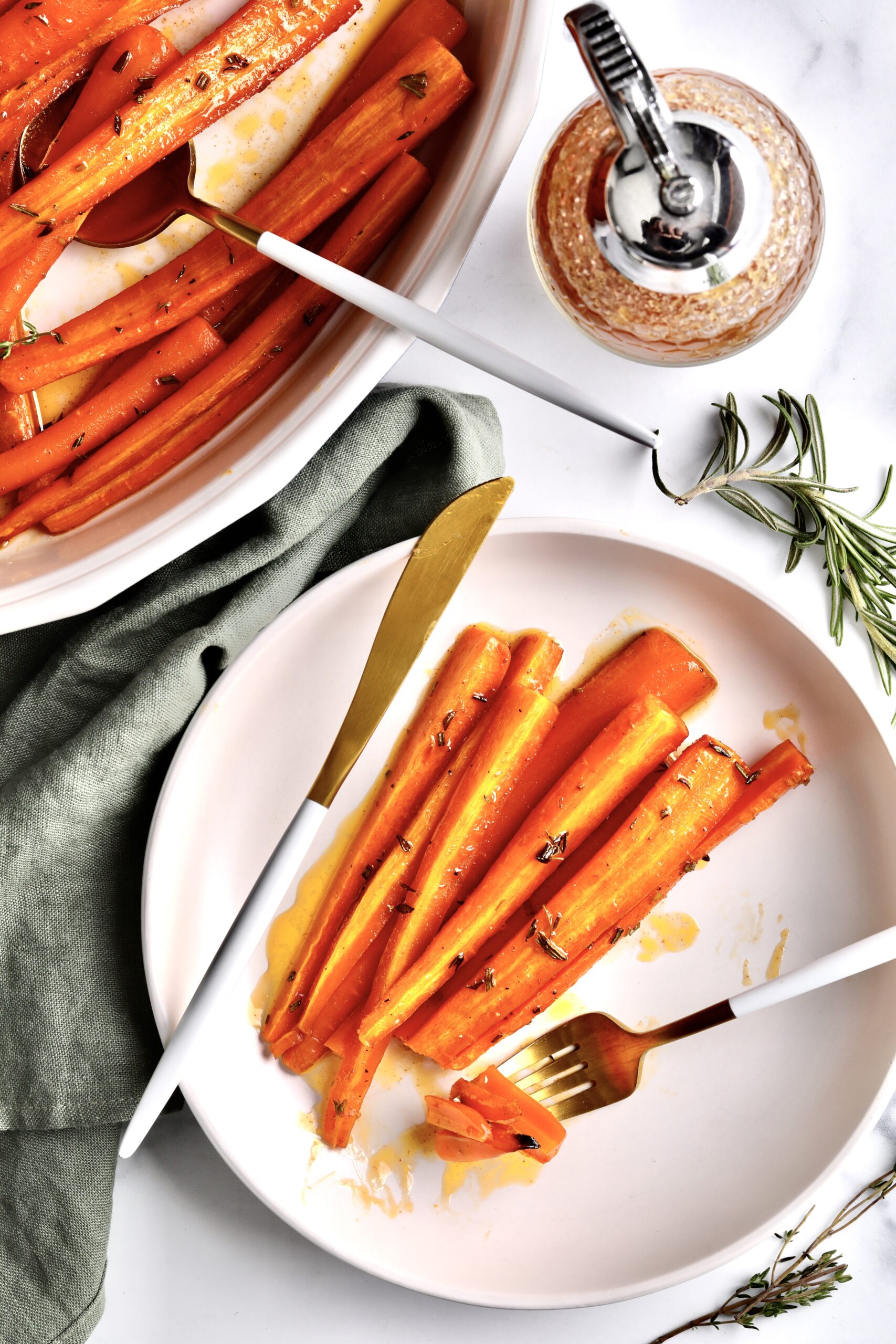 Best Honey Glazed Carrots Recipe (Oven Roasted) on a plate with fork and knife. A jar of honey and herbs in the background.