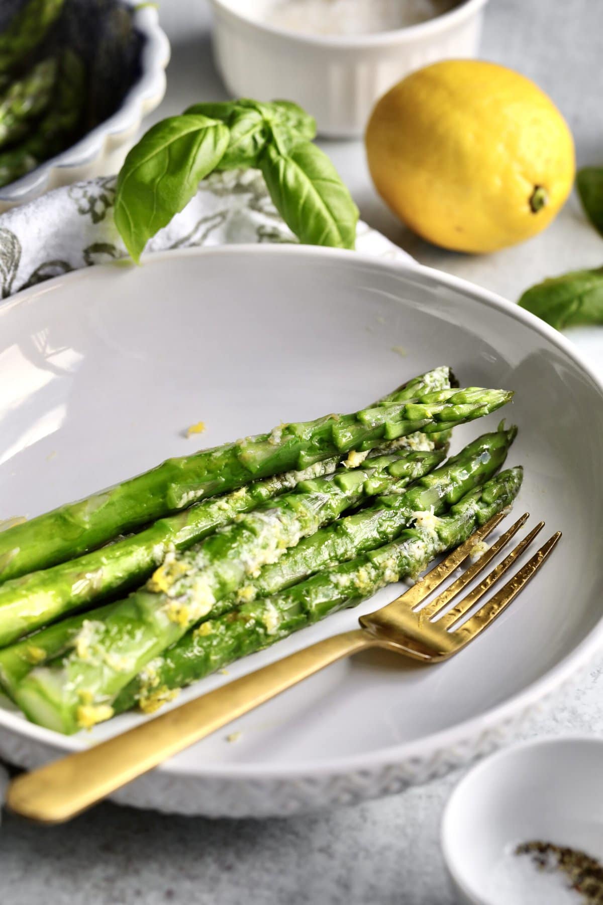 Simple Steamed Asparagus Recipe (Quick and Easy) on a plate with a fork. Lemon and basil as garnish.