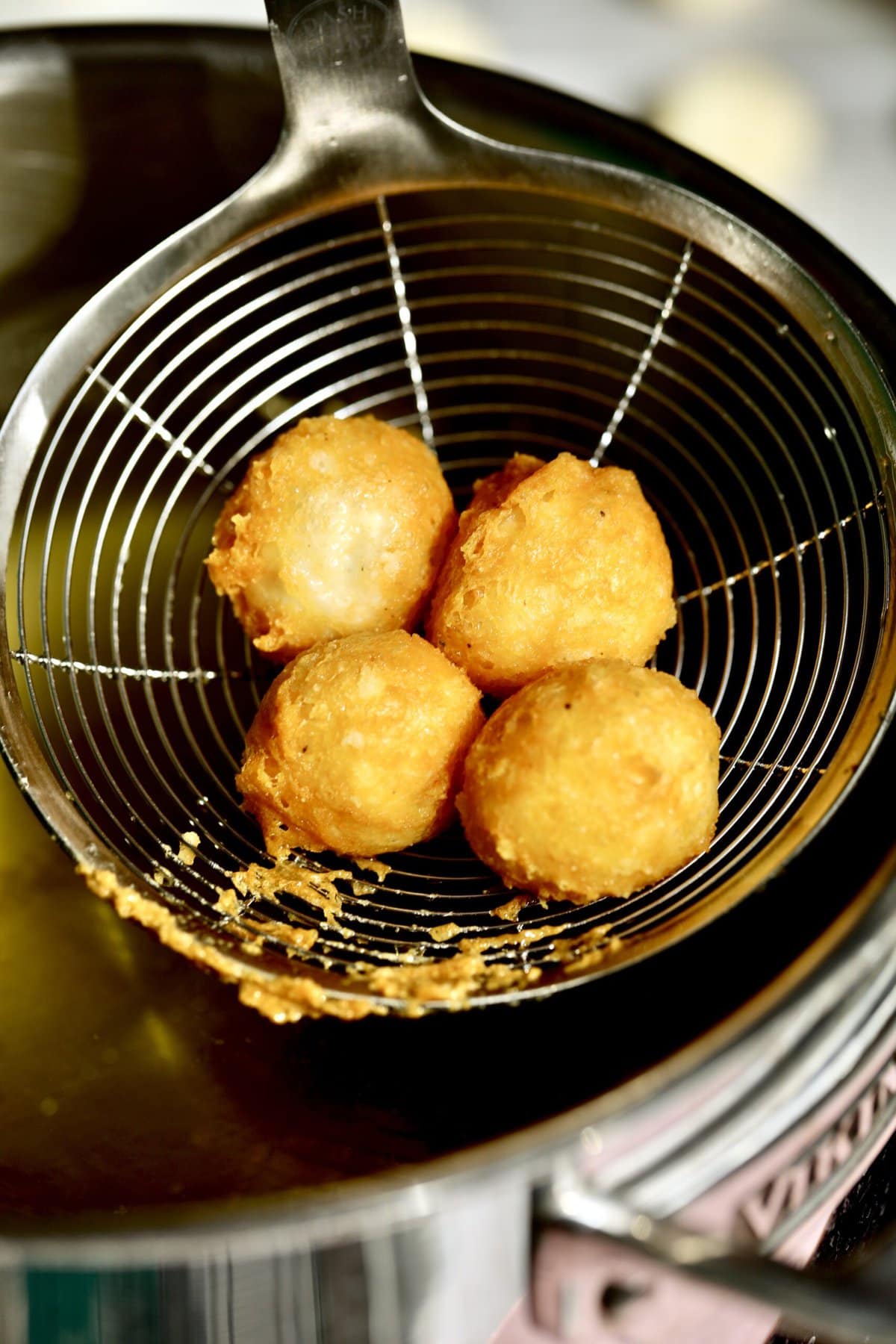 Process for making fried cheese balls- taking the cheese balls out of the fryer with slotted spoon.