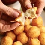 hands opening a fried cheese ball to show the gooey cheese interior.