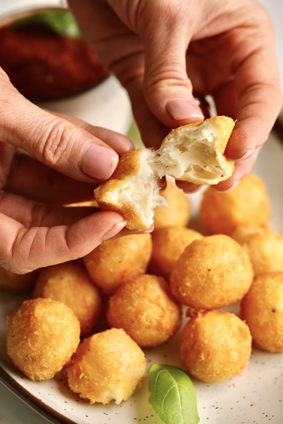 hands opening a fried cheese ball to show the gooey cheese interior.