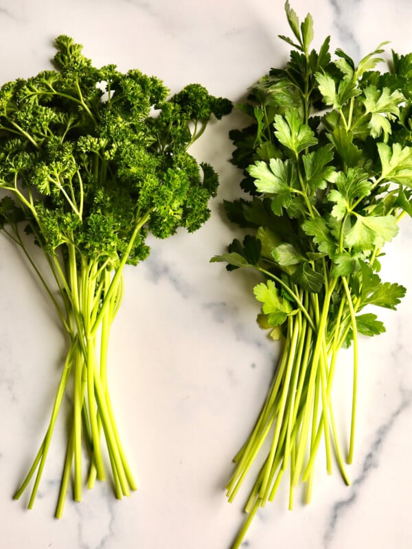 Bunches of parsley and Italian parsley on a marbled surface.