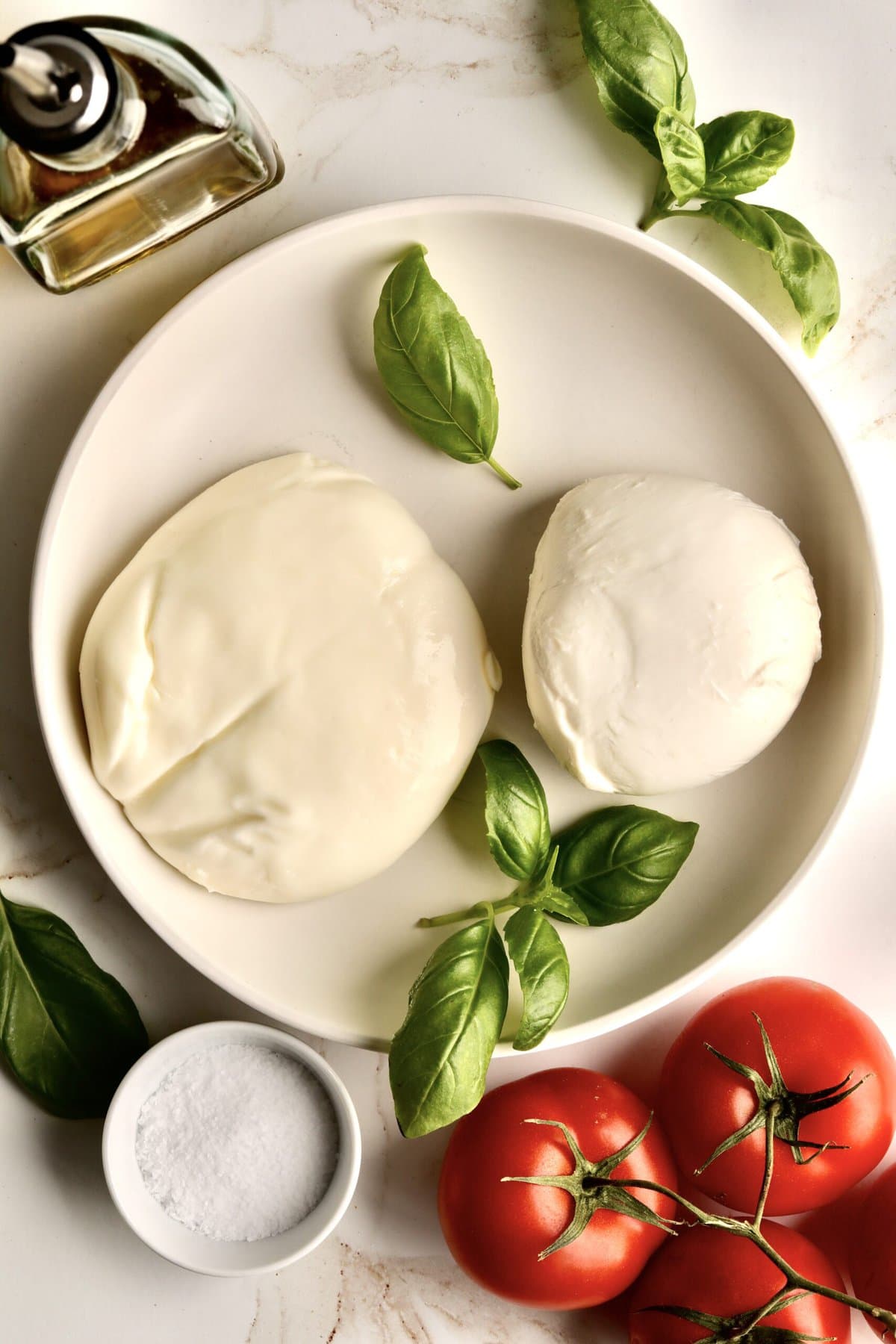 mozzarella and burrata cheese on a white plate with basil leaves.