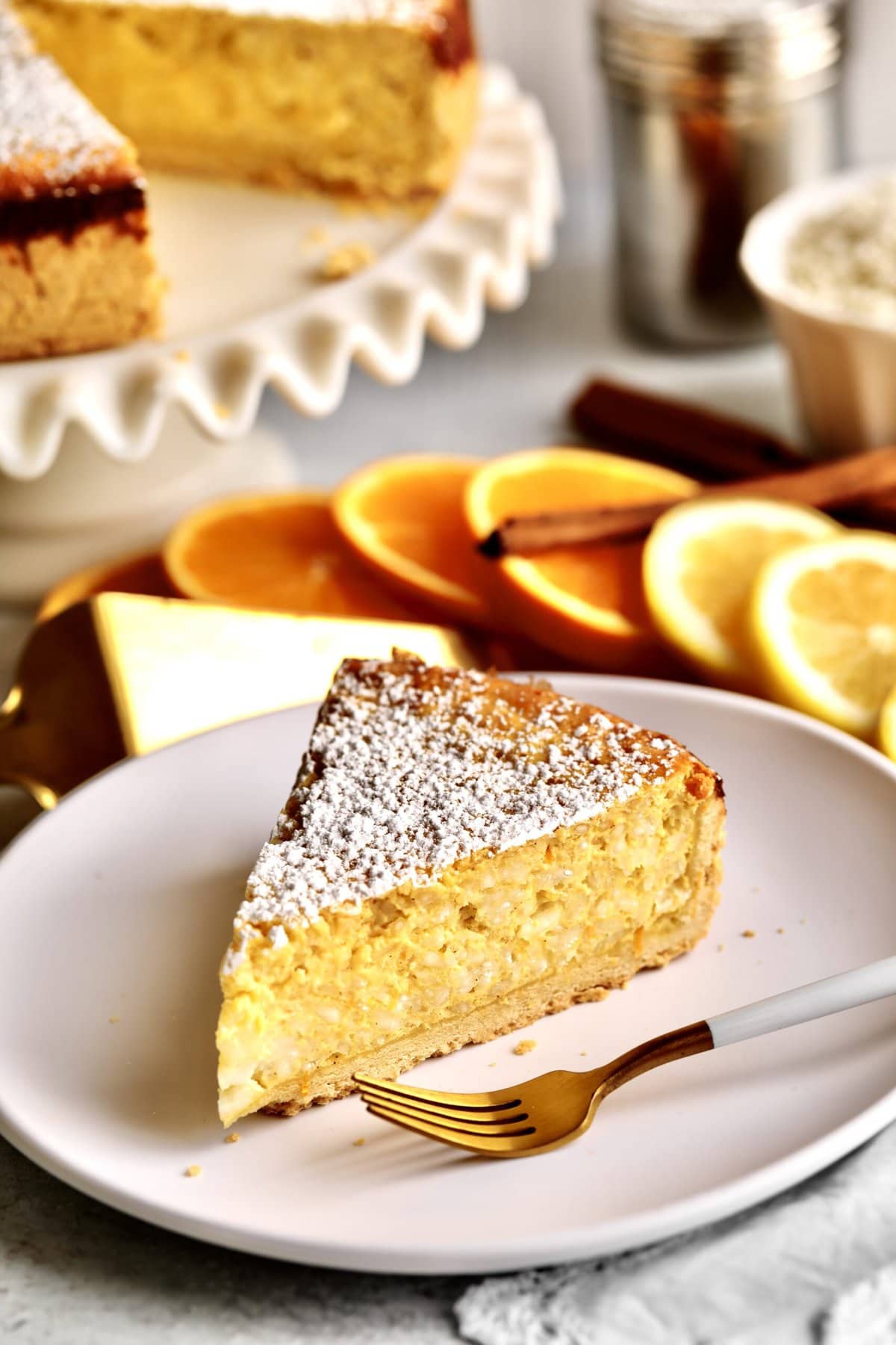 Italian Easter Rice Pie Recipe (Pastiera di Riso)-  big slice on a plate. Slices of oranges in the background. Full cake in the background. 
