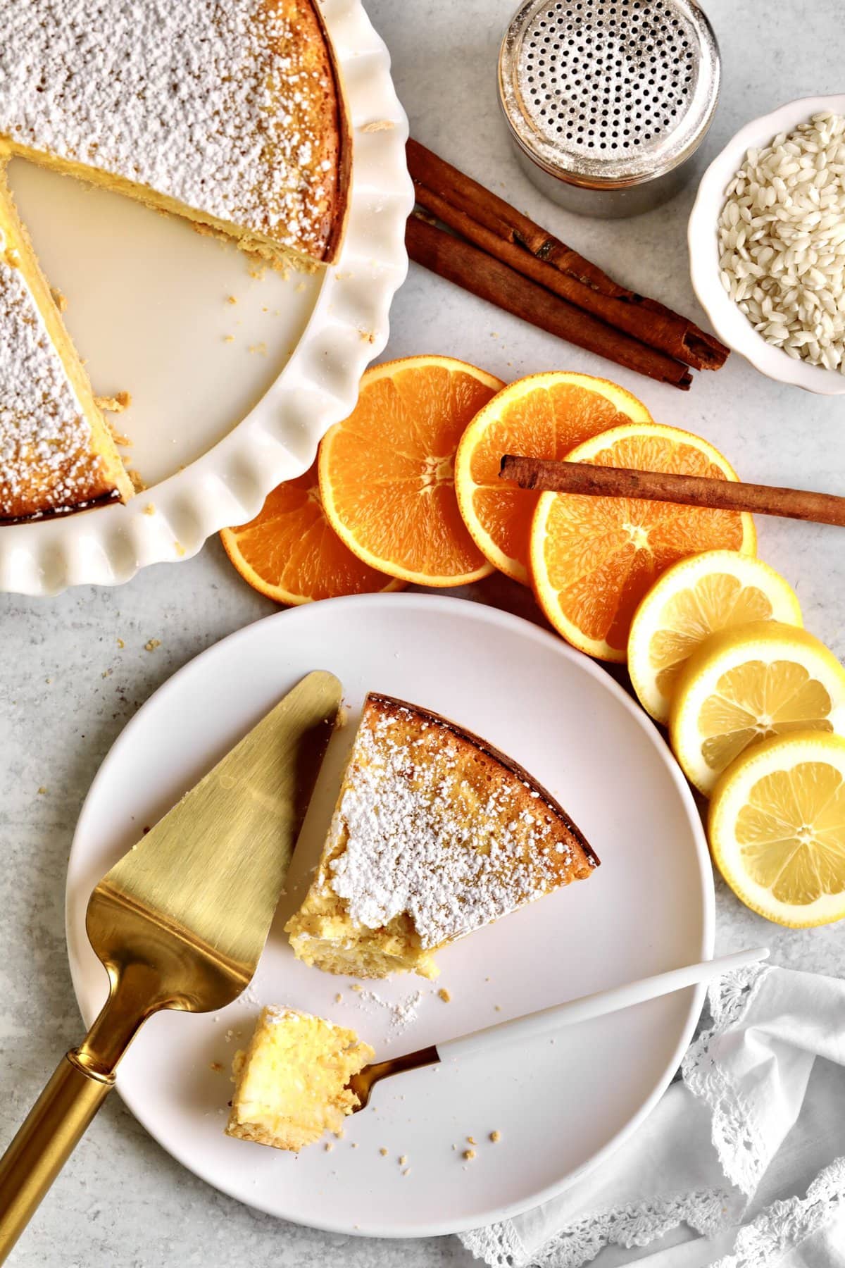 Italian Easter Rice Pie Recipe (Pastiera di Riso)- big slice on a plate with a bite taken out. Slices of oranges in the background. Full cake in the background.