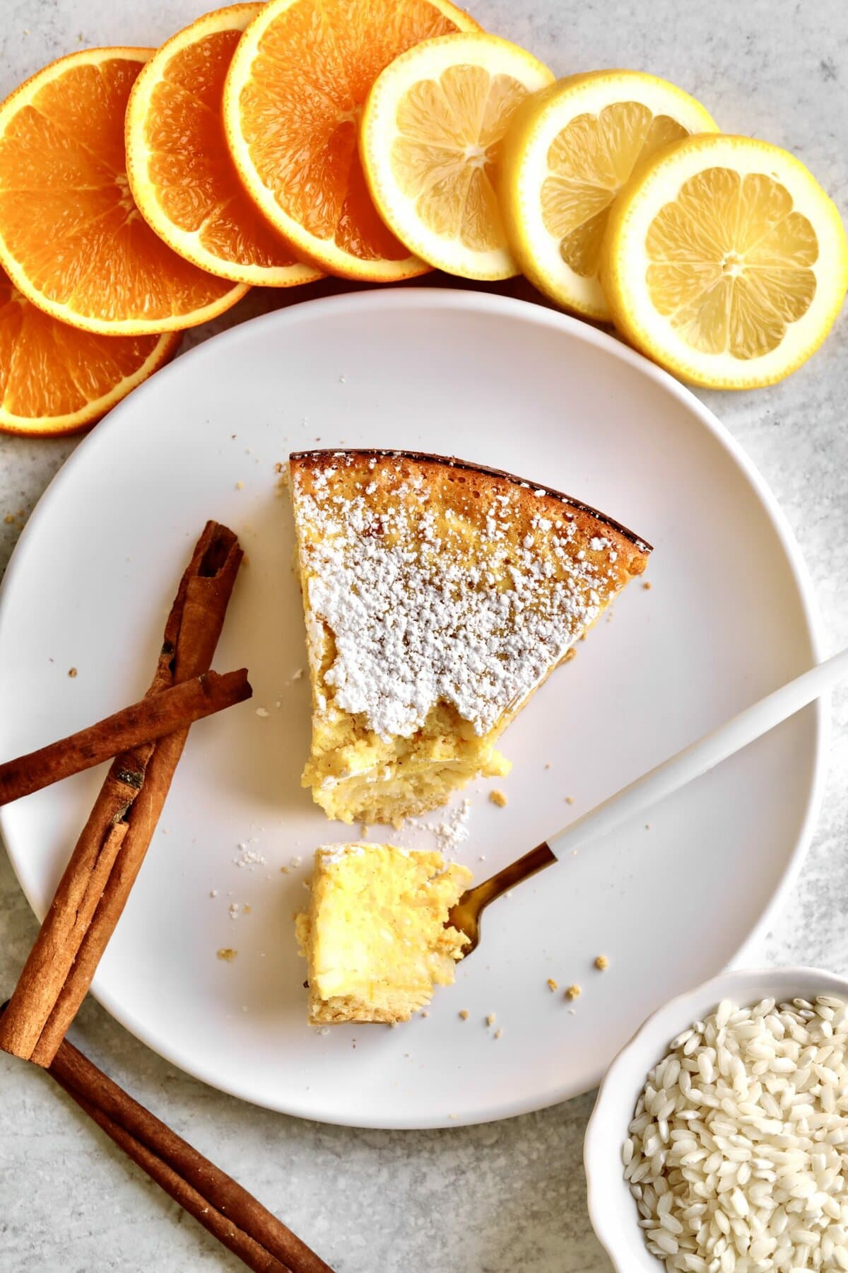 Italian Easter Rice Pie Recipe (Pastiera di Riso)- on a plate with orange and lemon slices and cinnamon sticks surrounding plate.