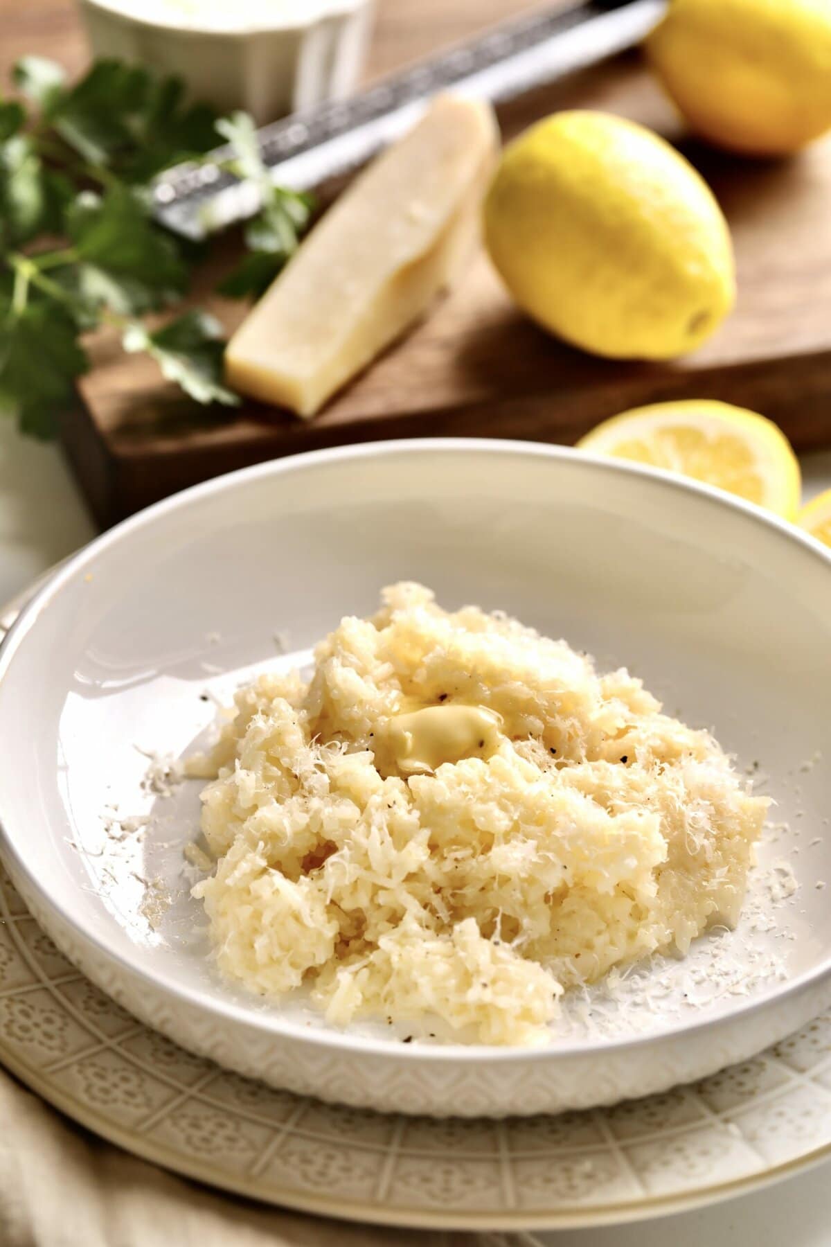 creamy rice on a plate with lemon and a block of parmigiano cheese in the background.