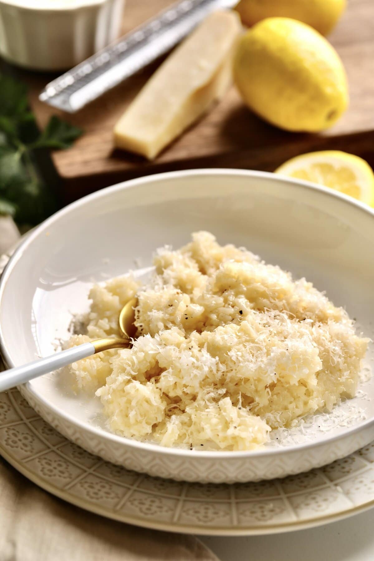creamy rice on a plate with lemon and a block of parmigiano cheese in the background.