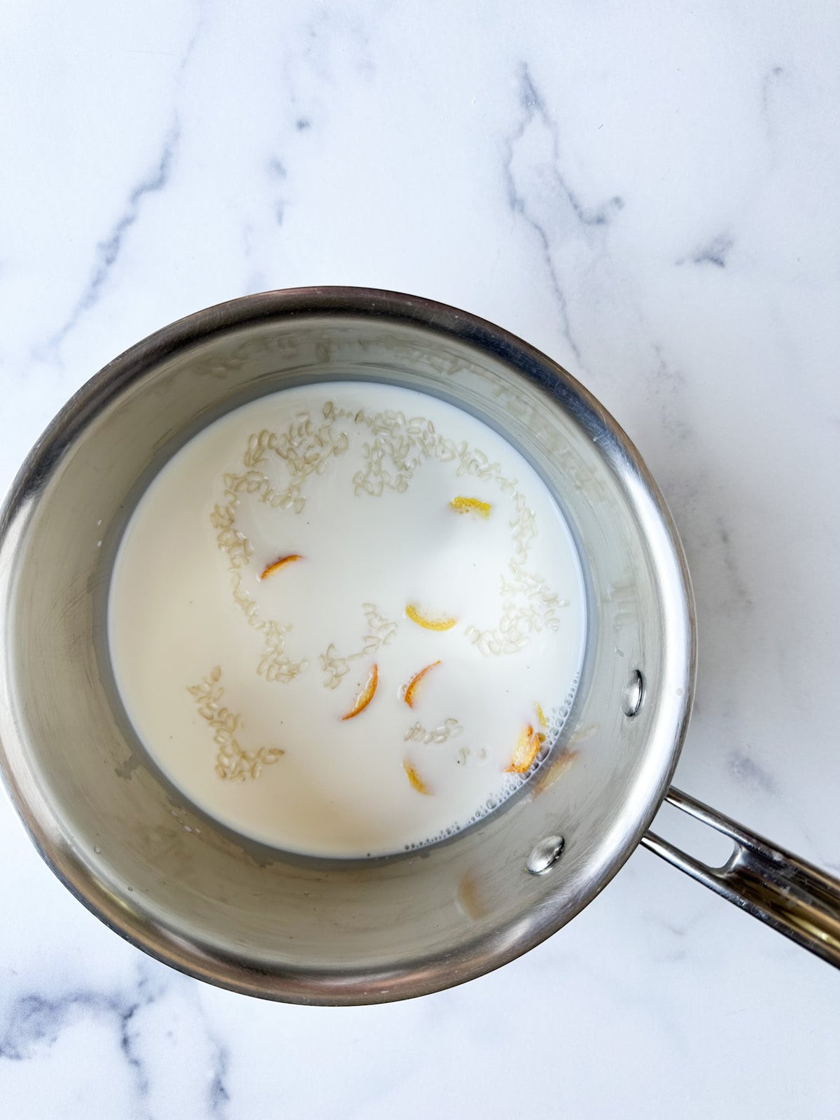 rice in milk with lemon and orange peel in a pot ready to cook.