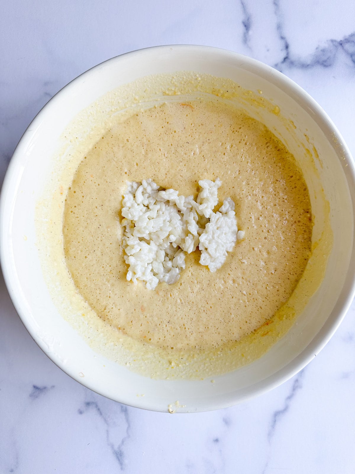 Adding rice to the egg and ricotta mixture in a mixing bowl.