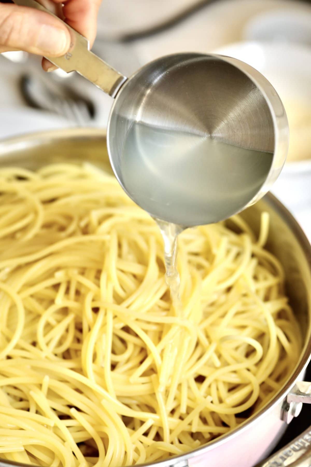 process for how to make spaghetti alla nerano- adding reserved pasta water to the pan with pasta and zucchini.