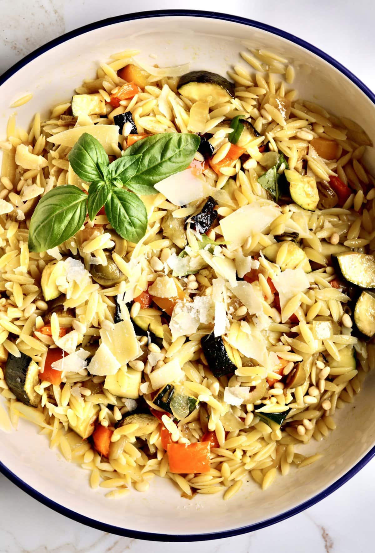 close up of easy orzo pasta with roasted veggies. Thick slices of Parmesan cheese on top. Basil to garish.