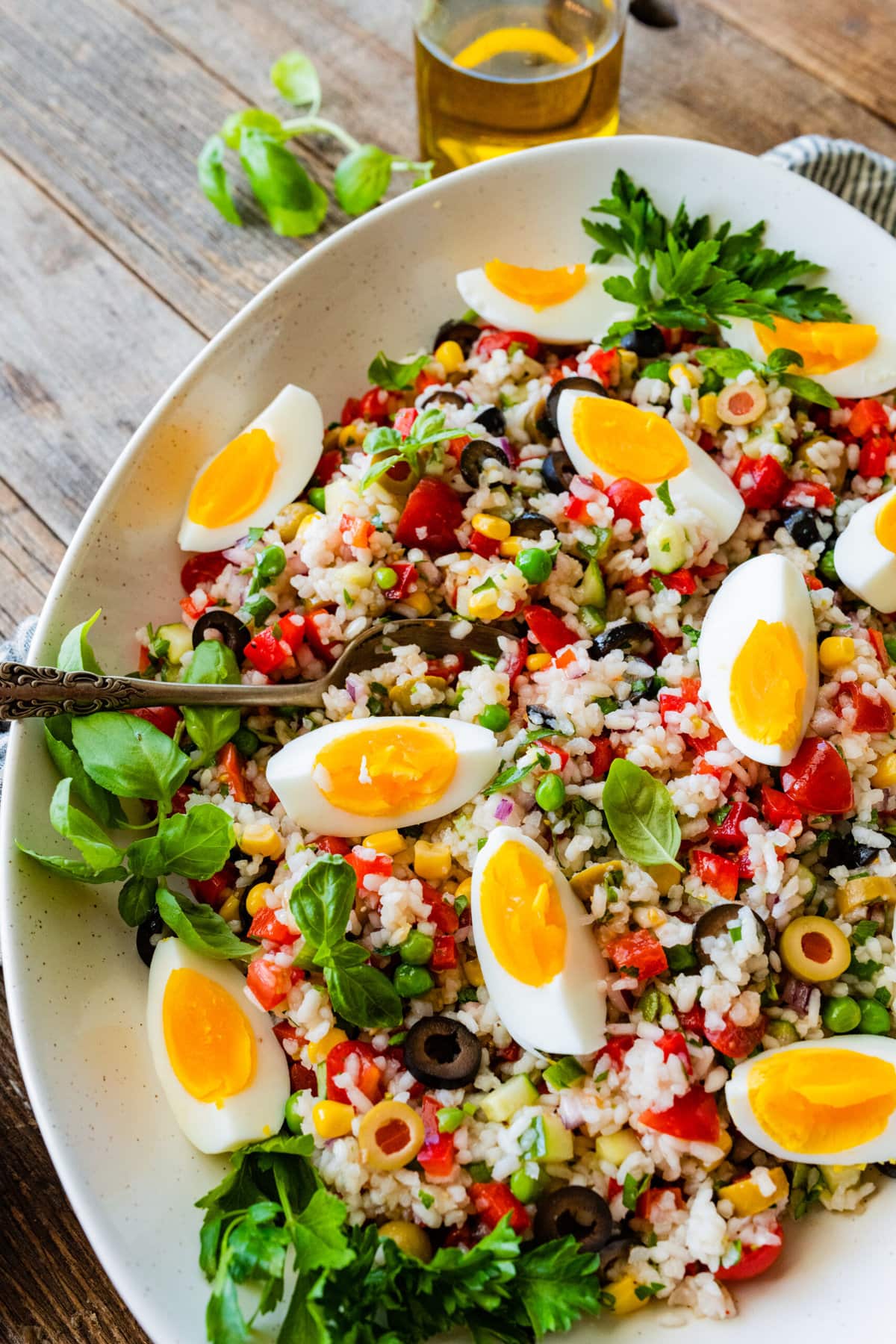 Easy Italian rice salad (insalata di riso) in a large platter with the hard boiled eggs sliced on top. Serving spoon in the platter ready to serve.