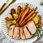 Lots of thick pork chop slices on a plate with potatoes and carrots.