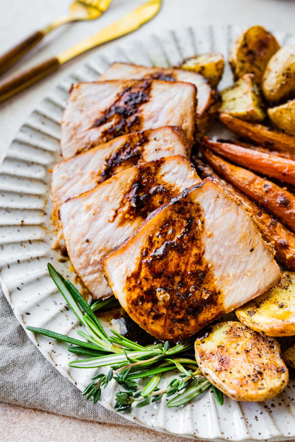 Lots of thick pork chop slices on a plate with potatoes and carrots. Pan sauce on top of thick pork chop slices.