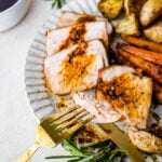 Lots of thick pork chop slices on a plate with potatoes and carrots. Bite taken out with a fork.