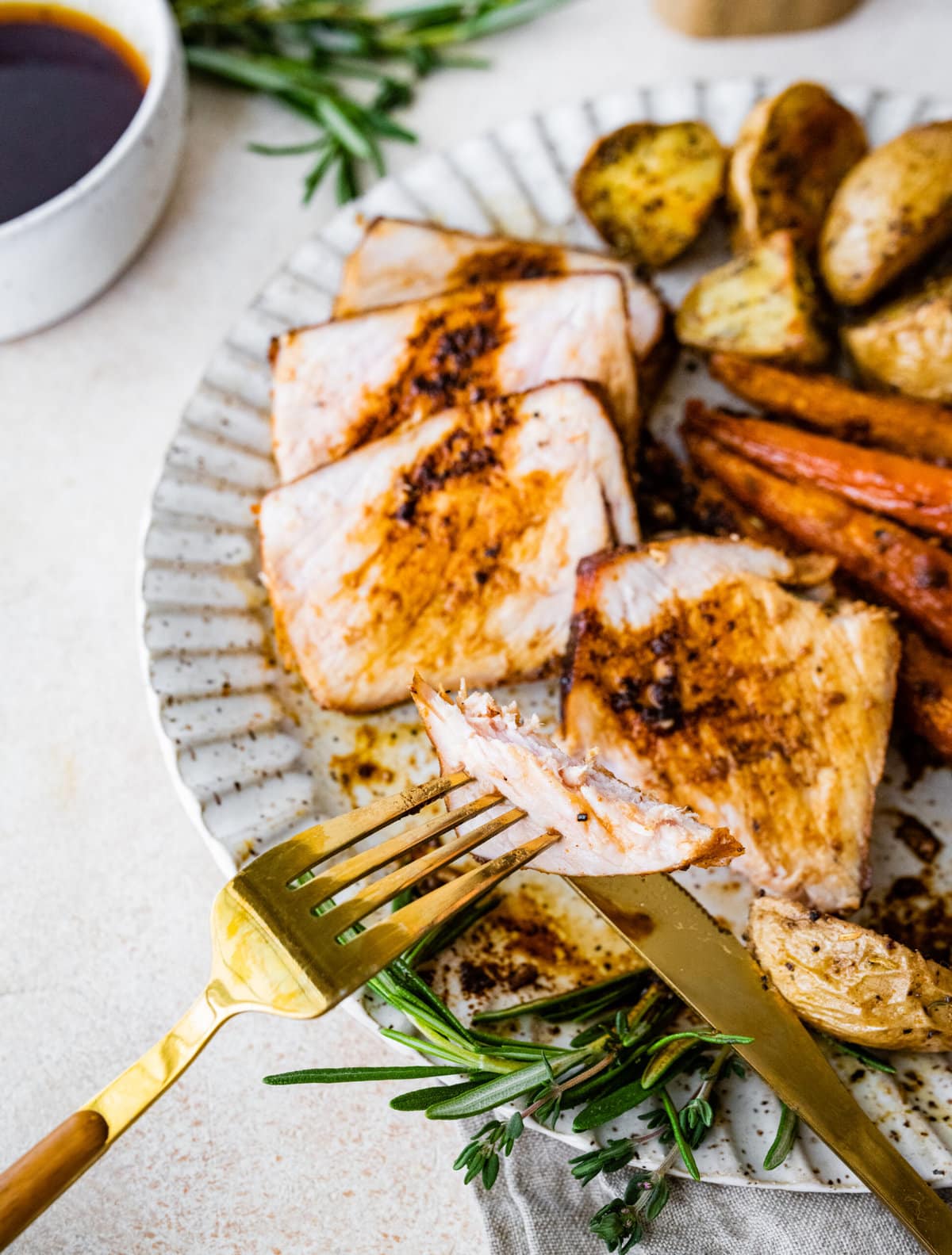 Lots of thick pork chop slices on a plate with potatoes and carrots. Bite taken out with a fork.