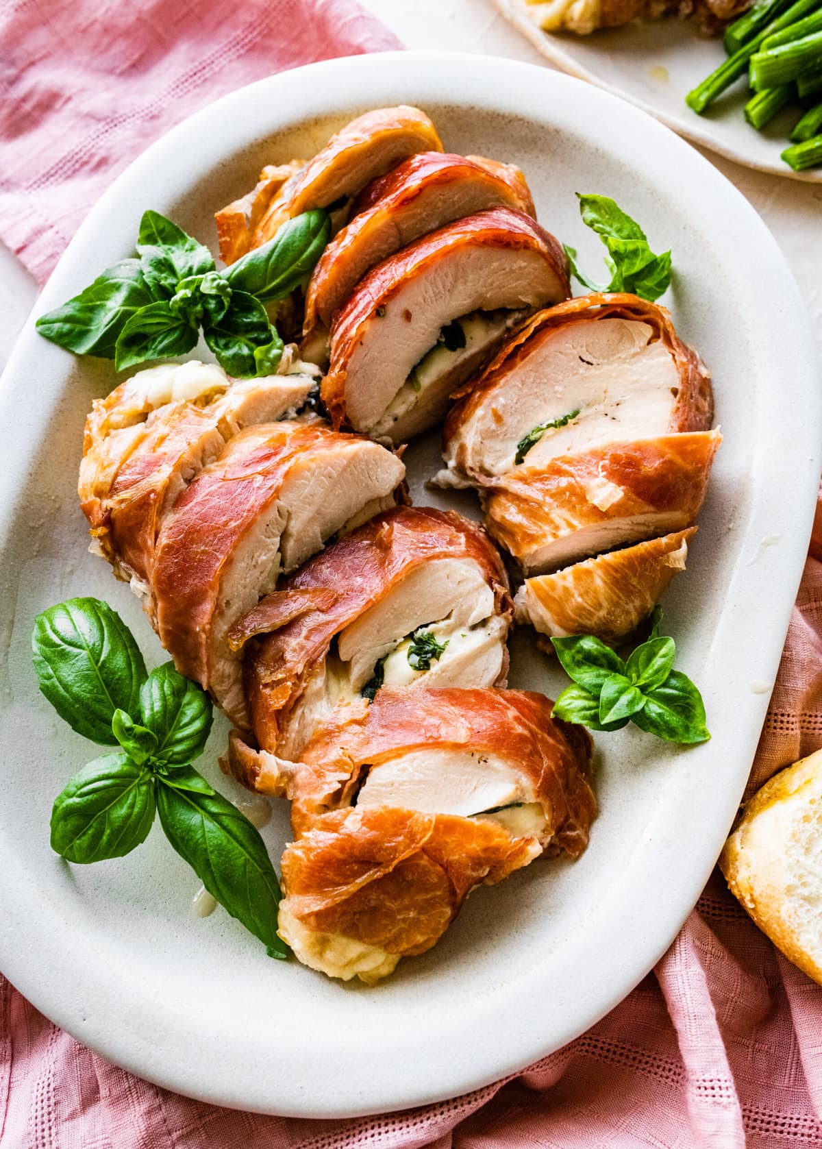 How to make Mozzarella stuffed Chicken chicken- finished stuffed chicken cut in slices and served on a white platter with fresh basil.