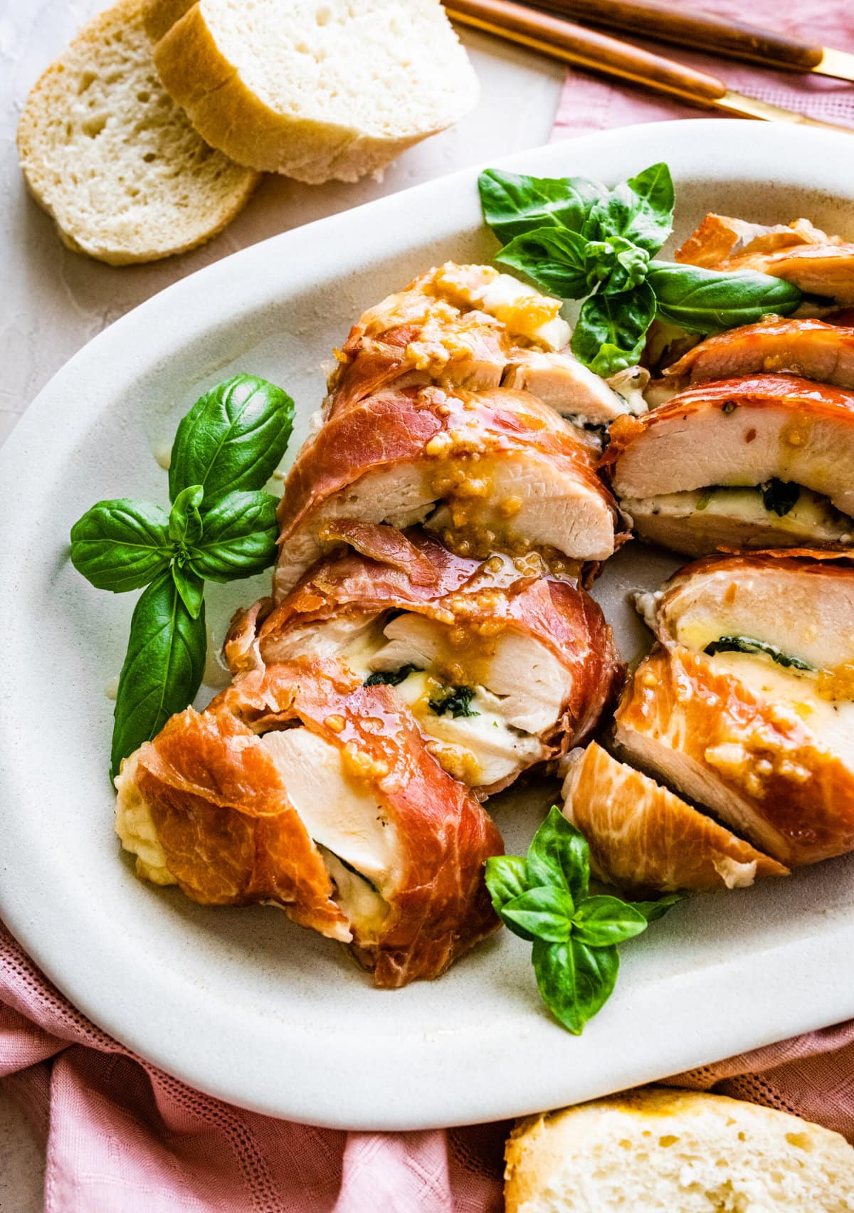 How to make Mozzarella stuffed Chicken chicken- finished stuffed chicken cut in slices and served on a white platter with fresh basil. Bread slices in background.