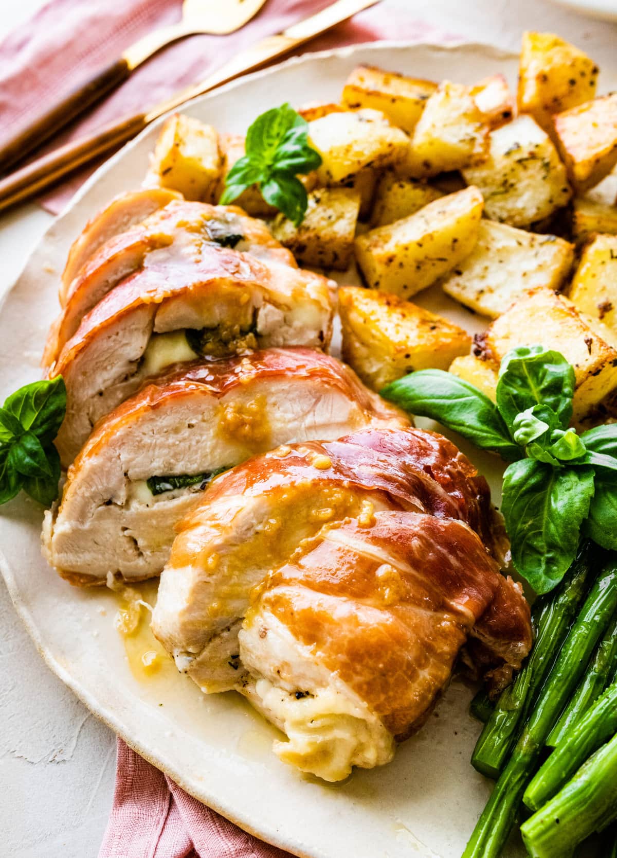 How to make Mozzarella stuffed Chicken chicken- finished stuffed chicken cut in slices and served on a white platter with fresh basil. Bread slices in background. Served with roasted potatoes and asparagus.