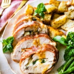 How to make Mozzarella stuffed Chicken chicken- finished stuffed chicken cut in slices and served on a white platter with fresh basil. Bread slices in background. Served with roasted potatoes and asparagus.