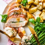 Mozzarella stuffed chicken, roasted potatoes, and asparagus on a plate with silverware.