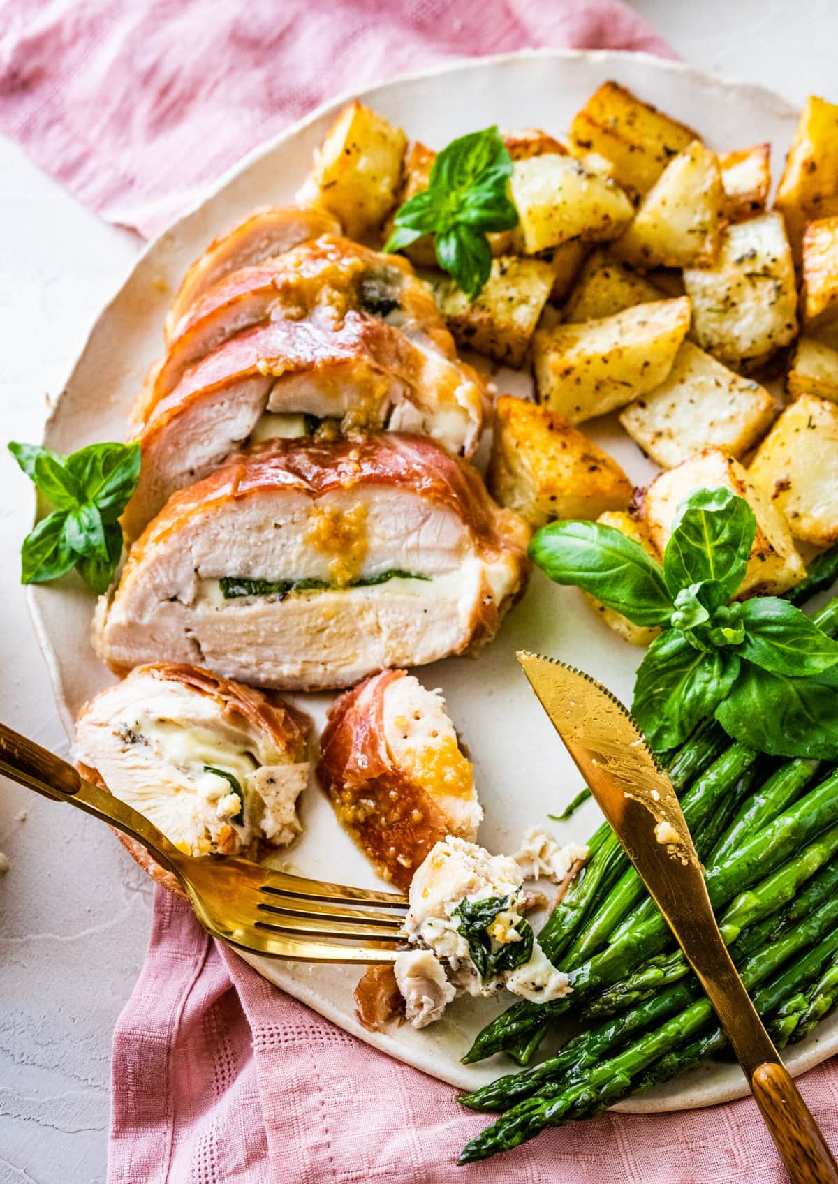 How to make Mozzarella stuffed Chicken chicken- finished stuffed chicken cut in slices and served on a white platter with fresh basil and drizzled with pan sauce. Bread slices in background. Served with roasted potatoes and asparagus.