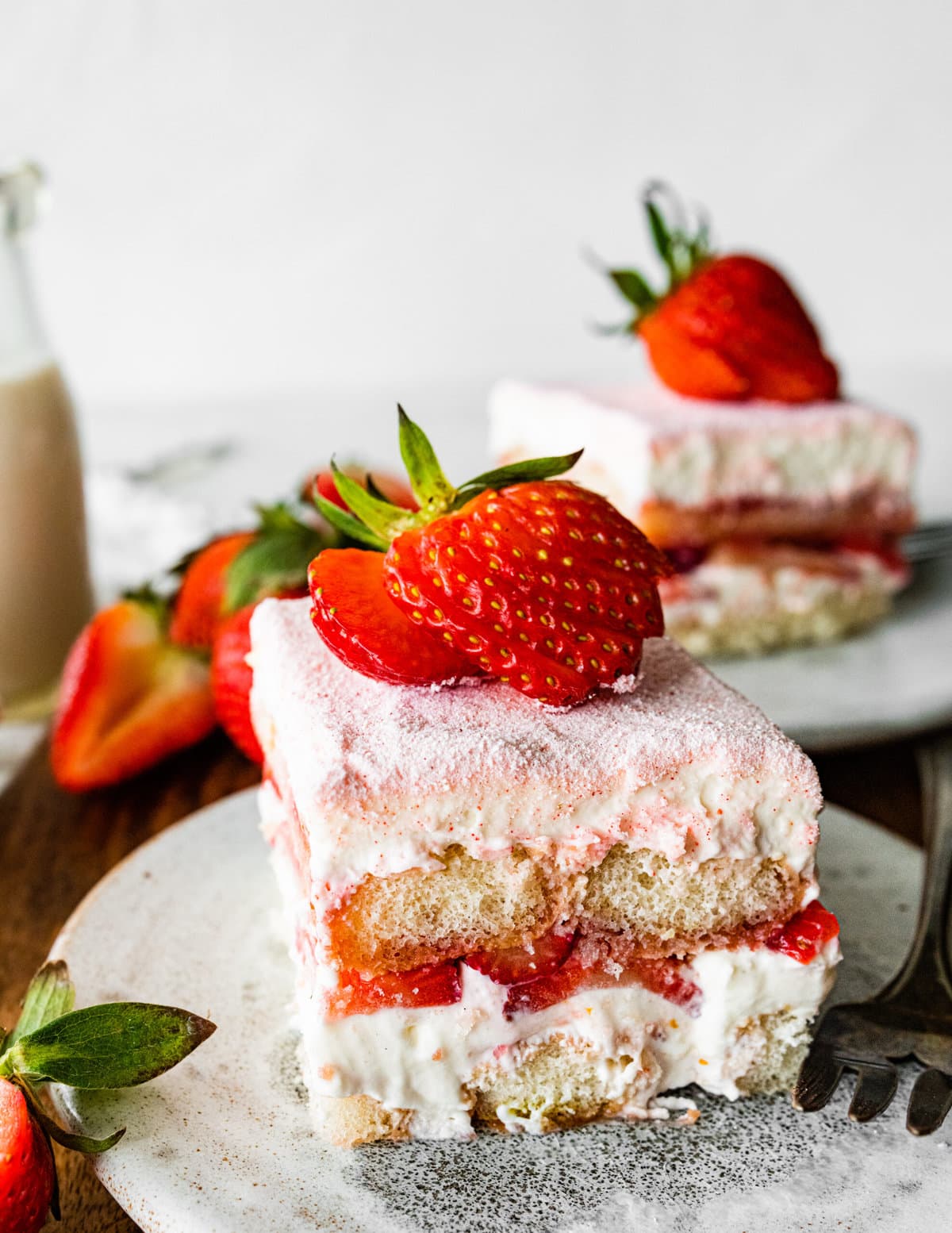 Single slice of the strawberry tiramisu on a plate with a sliced strawberry on top on a plate.