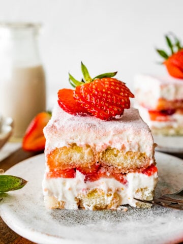 Single slice of the strawberry tiramisu on a plate with a sliced strawberry on top on a plate.