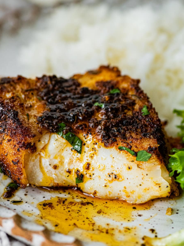 Blackened cod on a white place with rice and greens