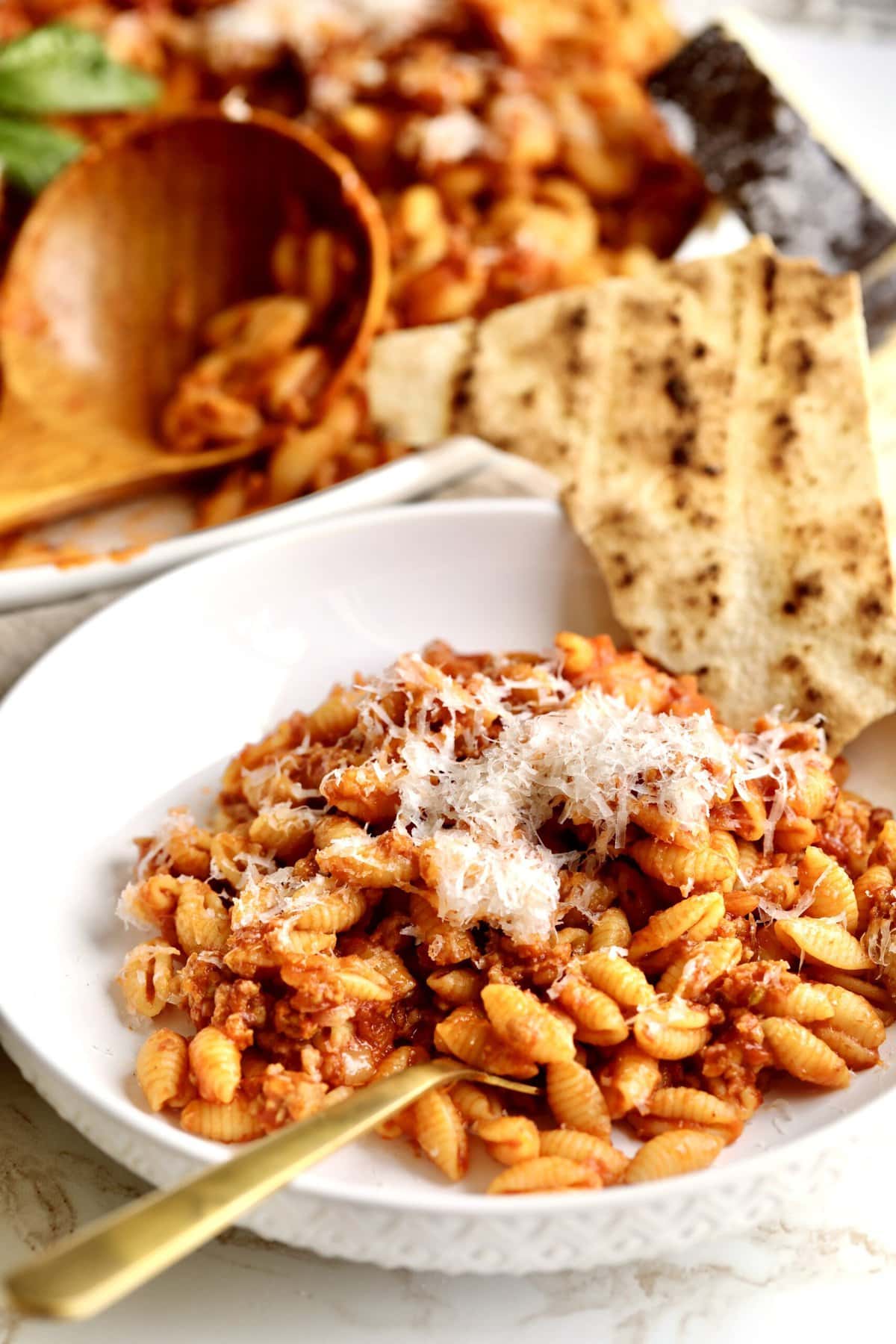 Malloreddus alla Campidanese (Sardinian Pasta with Sausage)in a bowl with a fork ready to eat. Side of Sardinian flat bread. 