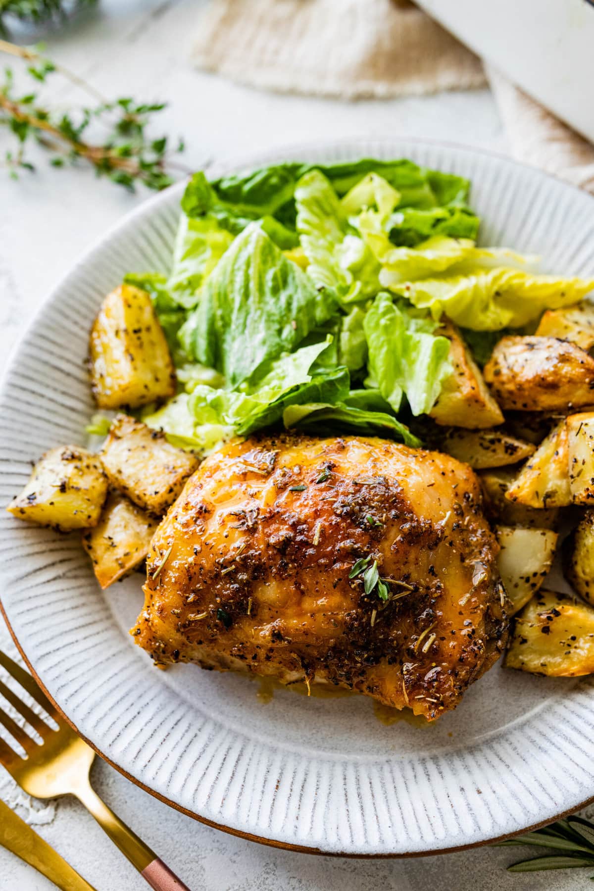 chicken thighs on a plate with salad and roasted potatoes. 