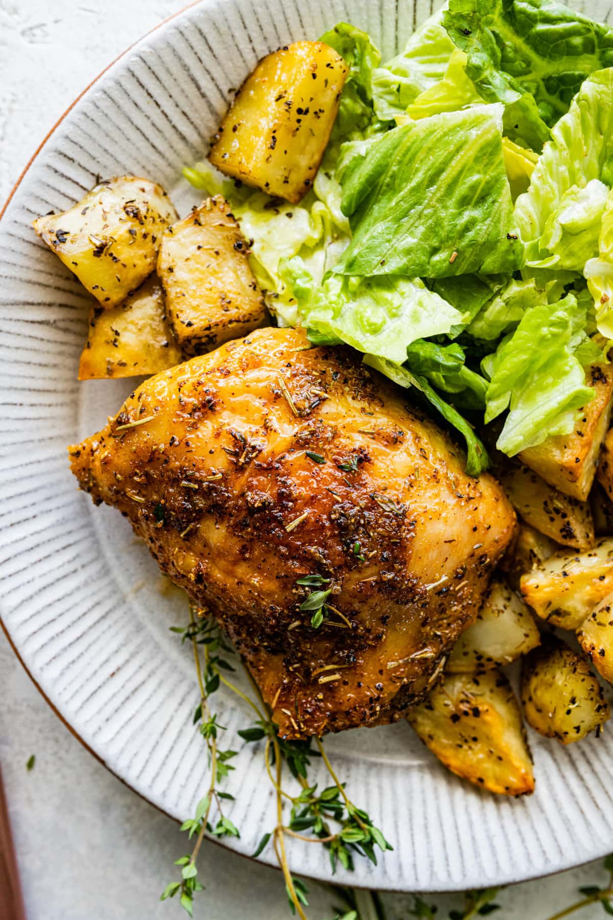 chicken thighs on a plate with salad and roasted potatoes.