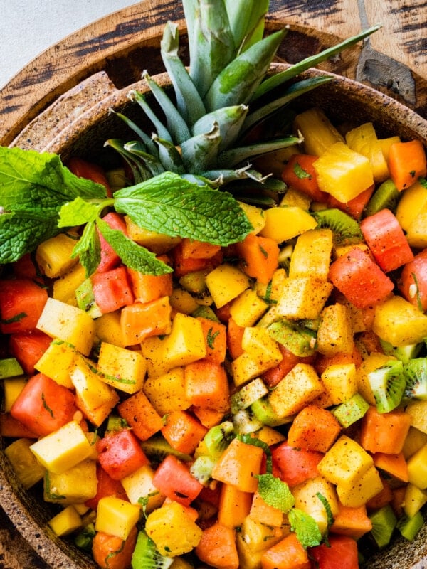 Big bowl of Best and Easy Mexican Fruit Salad in a large serving bowl with mint on top. Top of pineapple added for a festive twist. Papaya halves around the bowl.