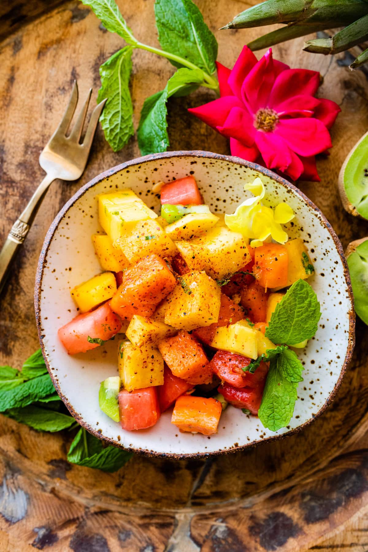 Best and Easy Mexican Fruit Salad in a serving bowl with festive flowers around the bowl with mint and kiwi.